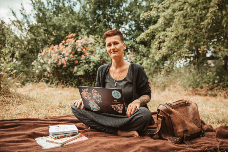 Die Autorin sitzt im Garten auf einer Decke mit dem Laptop auf dem Schoß
