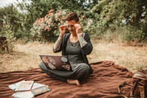 Die Autorin sitzt auf einer Decke im Garten, den Laptop auf dem Schoß